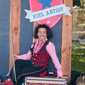 Lachender Artist in roter Weste mit Stock vor dem Kiel Artist Schild, Kieler Woche 2025