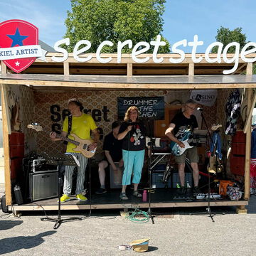 Band mit Bass, Gesang und Gitarre auf der secret stage mit Kiel Artist Schild, Kieler Woche 2025