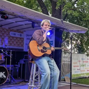 Sänger mit Akustikgitarre auf der Bühne des Offenen Kanals, secret stage, Kieler Woche 2025