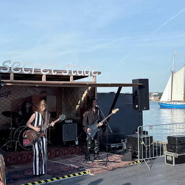 Band auf der secret stage an der Förde, im Hintergrund ein Segelschiff, Kieler Woche 2025