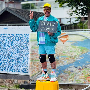 Straßenkünstler mit gelbem Helm hält ein Schild mit der Aufschrift Show Time, Kiel Artist, Kieler Woche 2025