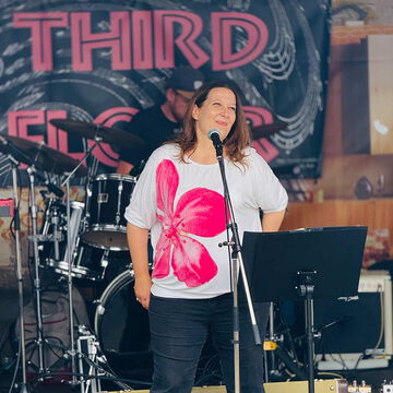 Sängerin im weißen Shirt mit Blumenmotiv am Mikrofon, secret stage, Kieler Woche 2025