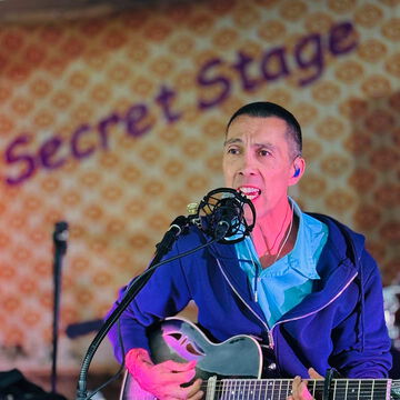 Sänger in blauer Jacke mit E-Gitarre vor dem secret stage Schriftzug, Kieler Woche 2025